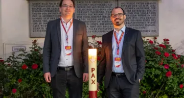 Übergabe der Ökumenischen Friedenskerze im Rahmen der Langen Nacht der Kirchen 2023 von der Evangelisch-methodistischen Kirche Linz zur Evangelischen Pfarrgemeinde A.B. Linz – Innere Stadt. Am Bild: Pfarrer Wolfgang Ernst (links) und Pastor Martin Obermeir-Siegrist (rechts) vor der Martin-Luther-Kirche Linz